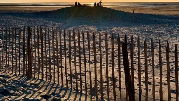A beach with a wooden fence in the foreground and people sitting on a sand dune in the background during sunset. - Villa touquettoise near the sea (Le Touquet-Paris-Plage)