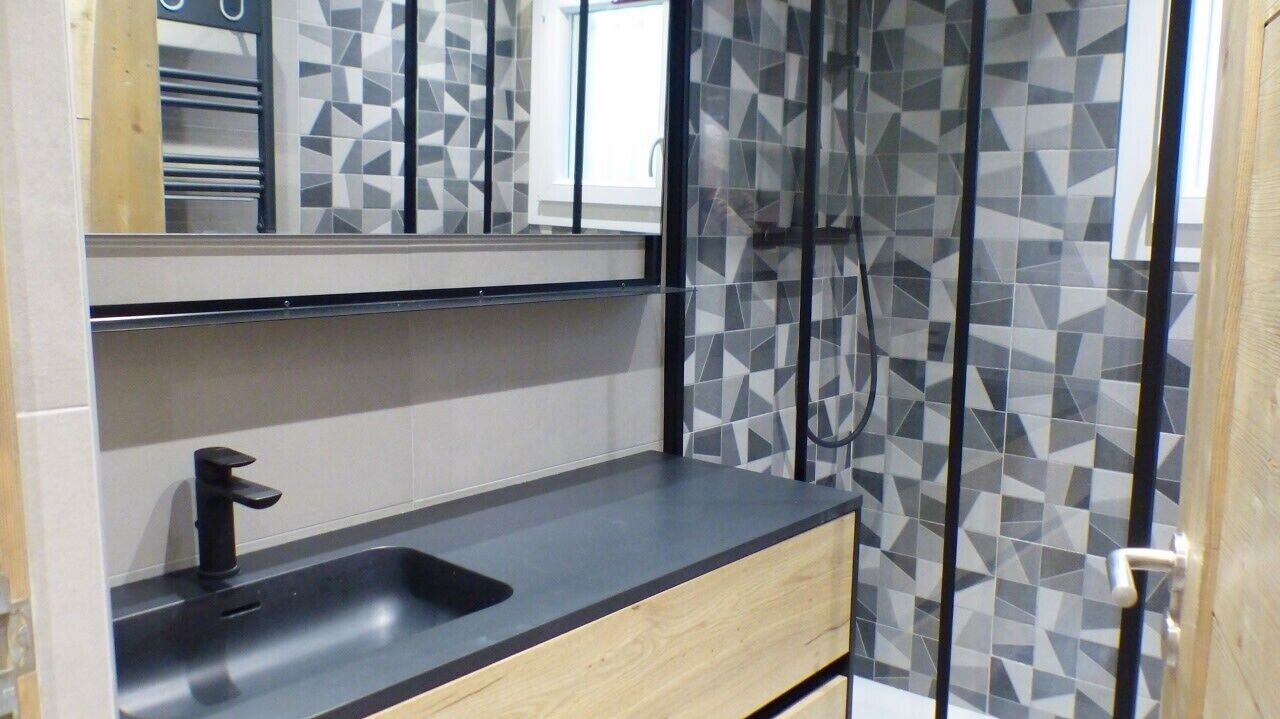 Un baño con lavamanos moderno, espejo y cabina de ducha con diseño geométrico.