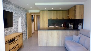 Una cocina moderna con armarios de madera y una isla integrada. Hay un televisor de pantalla plana montado en la pared y un mueble de madera con cajones.