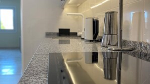 A modern kitchen with a stainless steel cooktop, a coffee machine, and a kettle on a granite countertop.