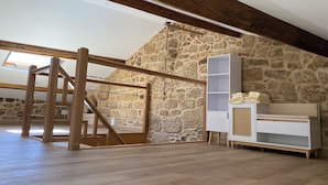 A loft bedroom with exposed wooden beams, a stone wall, and a wooden staircase.