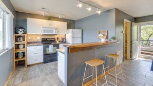 A modern kitchen with white cabinets, a wooden island with bar stools, and a view to the outside. - Lakefront Shell Knob Condo w/ Deck & Grill! (Shell Knob)