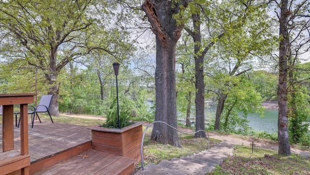 A wooden deck with steps leading to a seating area, surrounded by trees and a lake view. - Lakefront Shell Knob Condo w/ Deck & Grill! (Shell Knob)