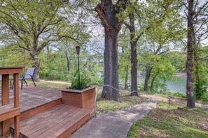 A wooden deck with steps leading to a seating area, surrounded by trees and a lake view. - Lakefront Shell Knob Condo w/ Deck & Grill! (Shell Knob)