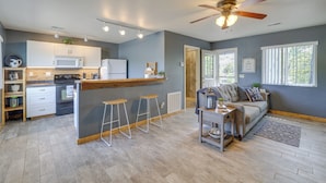 A modern kitchen with white cabinets, a wooden countertop, and a built-in microwave. There are three bar stools and a ceiling fan. The living area has a sofa, a coffee table, and a rug. - Lakefront Shell Knob Condo w/ Deck & Grill! (Shell Knob)