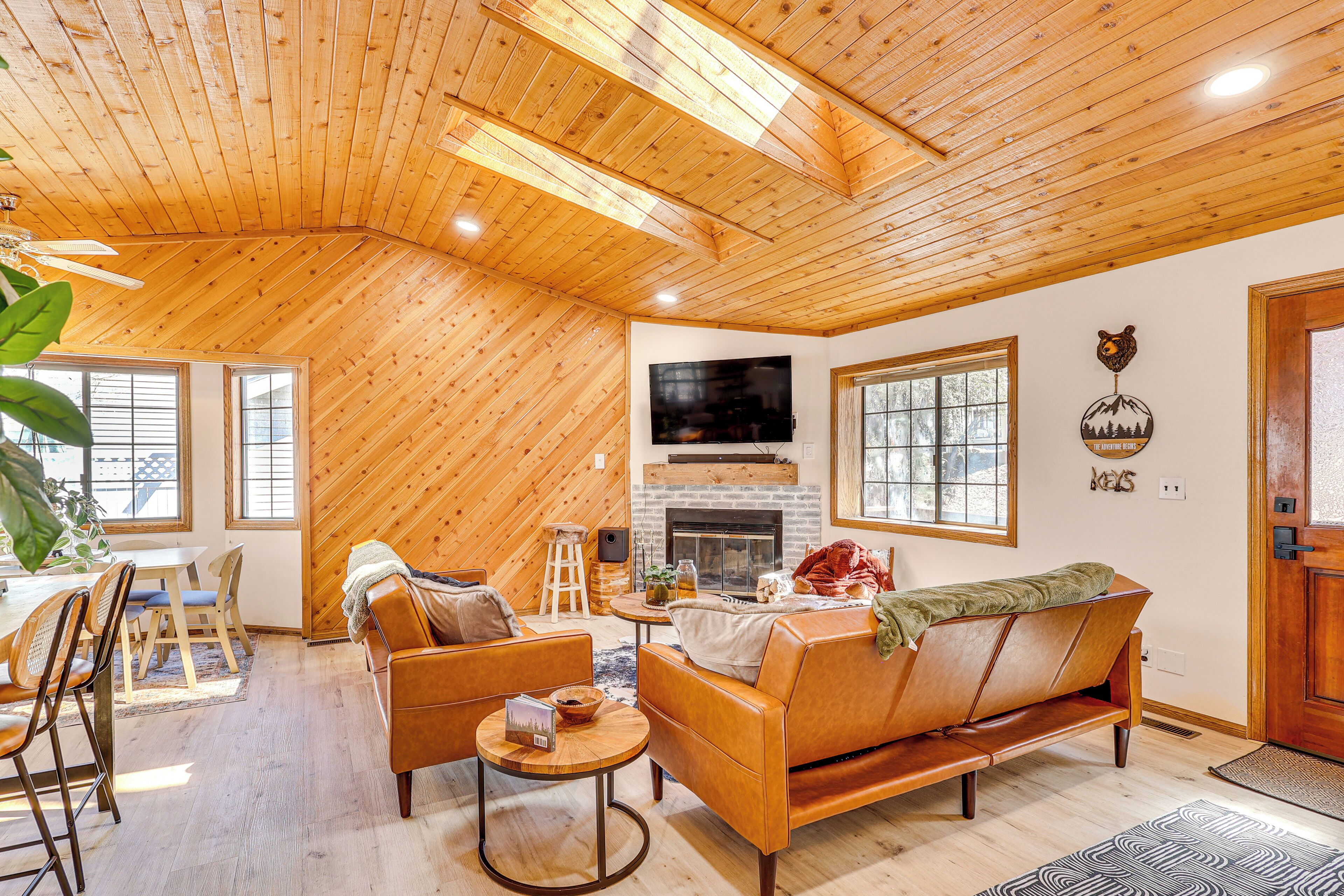 A cozy living room with a wooden ceiling, a fireplace, a sofa, and a TV mounted on the wall.