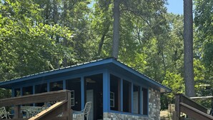 A cabin with a stone foundation, wooden deck, and a blue roof.