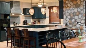 A modern kitchen with a large island, dark cabinetry, and pendant lighting.