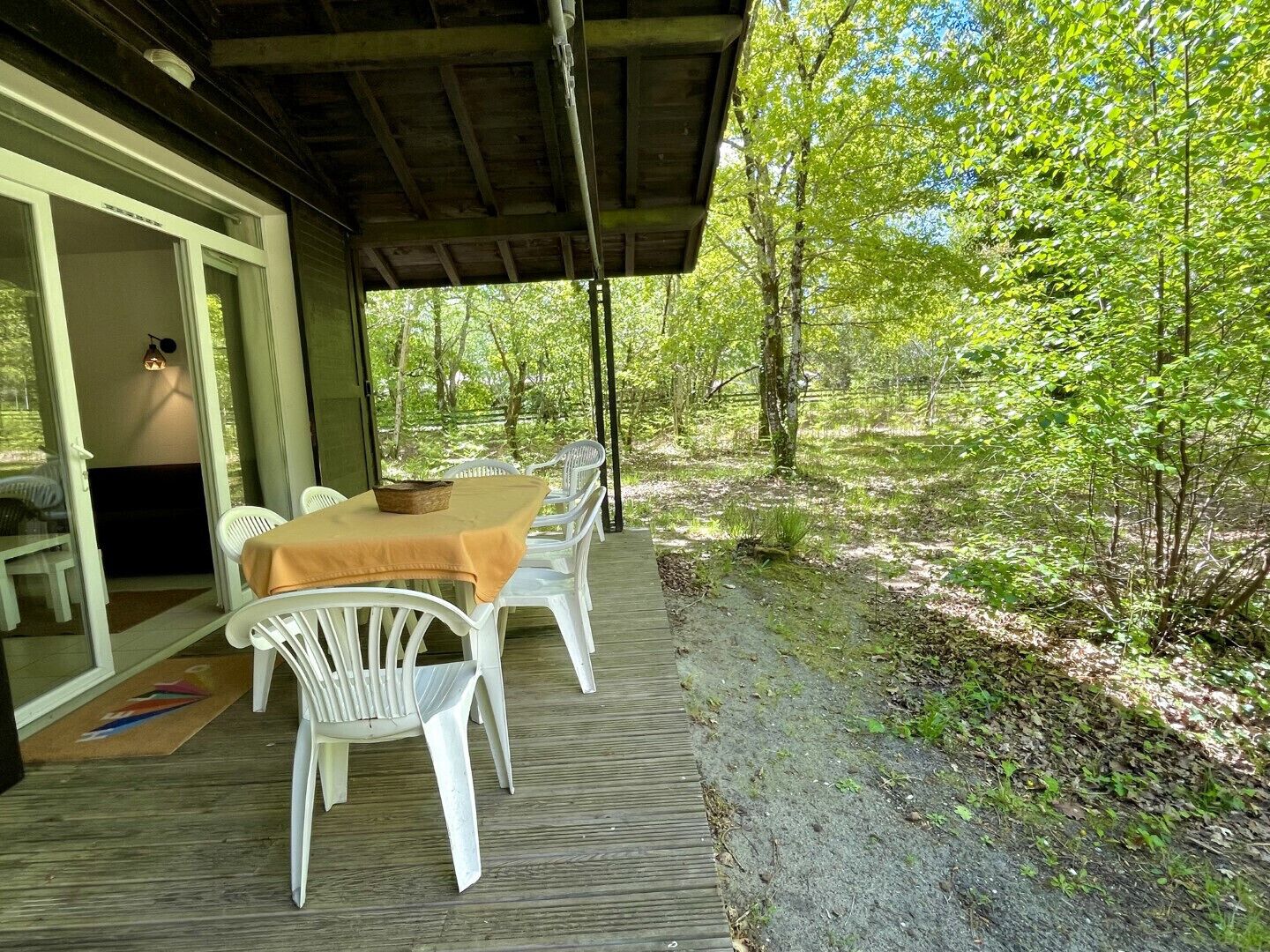 Un espace extérieur aménagé pour les repas, avec une table et des chaises, entouré d’une terrasse en bois et d’un paysage naturel.