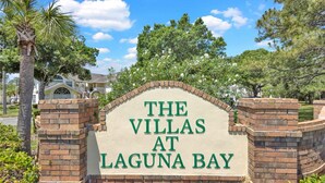A sign for "The Villas at Laguna Bay" with a brick archway and greenery in the background. - Disney Themed Condo mins from Disney attractions (Kissimmee)