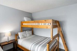 Een stapelbed met houten frame, een nachtkastje met lamp, en een effen muur.