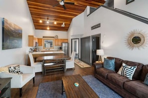 A modern living area with a dining table, sofa, and a kitchen in the background.