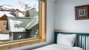 A bedroom with a bed, a window with a view of snow-covered mountains, and a framed picture on the wall. - Incredible Ski-Access: 3 Bed Chalet with HotTub (Big Sky)