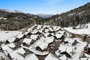 A snow-covered village with multiple cabins, surrounded by dense forests and mountains.