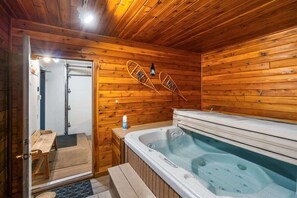 Interior de una cabaña de madera con jacuzzi, paredes de madera y un banco cerca de la puerta.