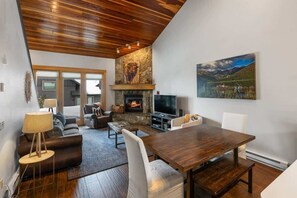 Una sala de estar moderna con chimenea de piedra, un televisor grande y un comedor con mesa y sillas de madera.