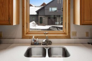 A kitchen with a double sink, wooden cabinets, and a window overlooking a snowy landscape.