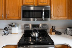 A kitchen with wooden cabinets, a stainless steel microwave, a stove with a kettle, and a toaster. - Incredible Ski-Access: 3 Bed Chalet with HotTub (Big Sky)