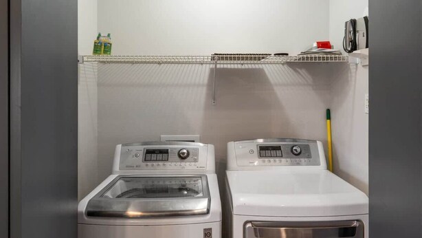 A laundry room with two stacked washers and dryers, a metal shelf with cleaning supplies, and a broom leaning against the wall. - Incredible Ski-Access: 3 Bed Chalet with HotTub (Big Sky)