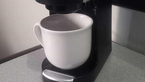 Een koffiezetapparaat met een witte mok op een aanrecht.