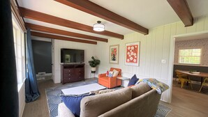 Una sala de estar con un televisor grande, un sofá, una mesa de centro y un comedor con mesa y sillas.