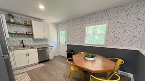 Una cocina moderna con armarios blancos, lavavajillas de acero inoxidable y una mesa de comedor de madera con sillas amarillas.