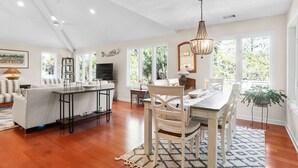 A spacious living room with a dining area, large windows, and a chandelier. - Pets  Considered, Community Pool, Lagoon View, Golf Cart Included 875 Salt Cedar Lane (Fripp Island)