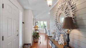 A hallway with a wooden floor, a decorative mirror, and a lamp on a console table. - Pets  Considered, Community Pool, Lagoon View, Golf Cart Included 875 Salt Cedar Lane (Fripp Island)