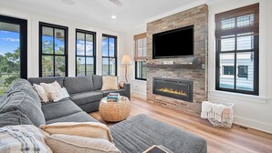 A modern living room with a fireplace, large windows, and a flat-screen TV. - Shuck Yeah - Brand New, Panoramic Marsh and Golf Views, Golf cart included 92 Davis Love (Fripp Island)
