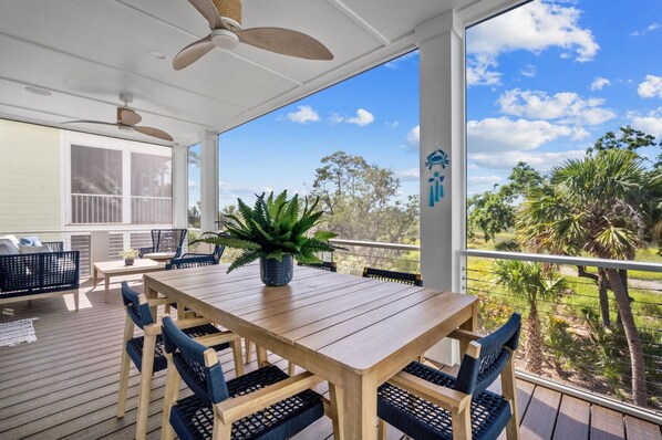 A covered outdoor area with a wooden table and chairs, a potted plant, and a view of trees and sky. - Shuck Yeah - Brand New, Panoramic Marsh and Golf Views, Golf cart included 92 Davis Love (Fripp Island)