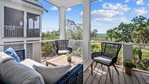 A covered outdoor deck with two wicker chairs and a sofa, overlooking a lush landscape. - Shuck Yeah - Brand New, Panoramic Marsh and Golf Views, Golf cart included 92 Davis Love (Fripp Island)