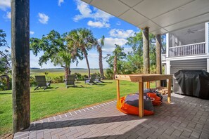 A covered patio with a table and chairs, a grill, and a view of a grassy field and trees. - Shuck Yeah - Brand New, Panoramic Marsh and Golf Views, Golf cart included 92 Davis Love (Fripp Island)