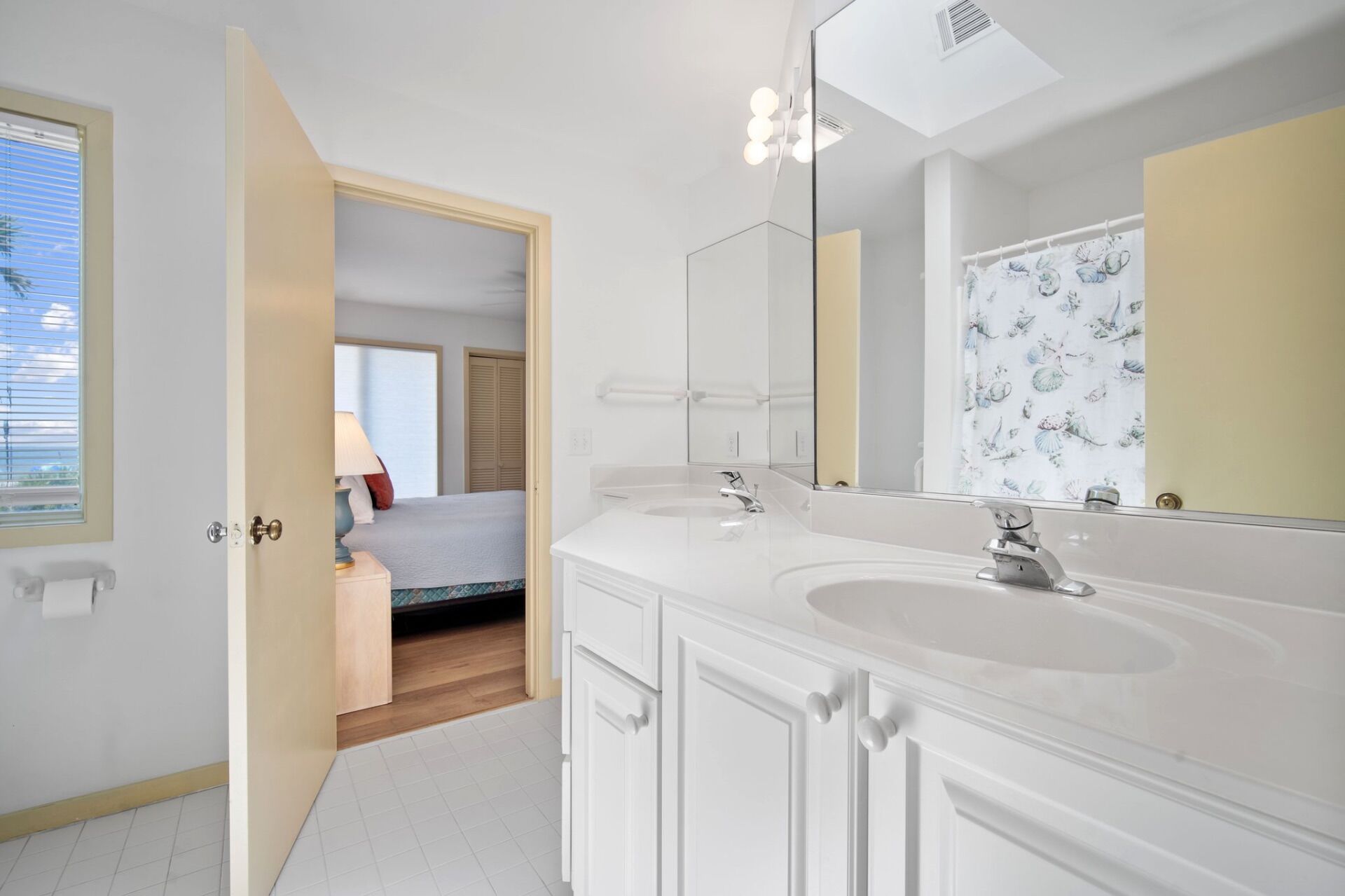 Une salle de bain moderne avec deux vasques, un grand miroir et un rideau de douche orné d’un motif de coquillages.
