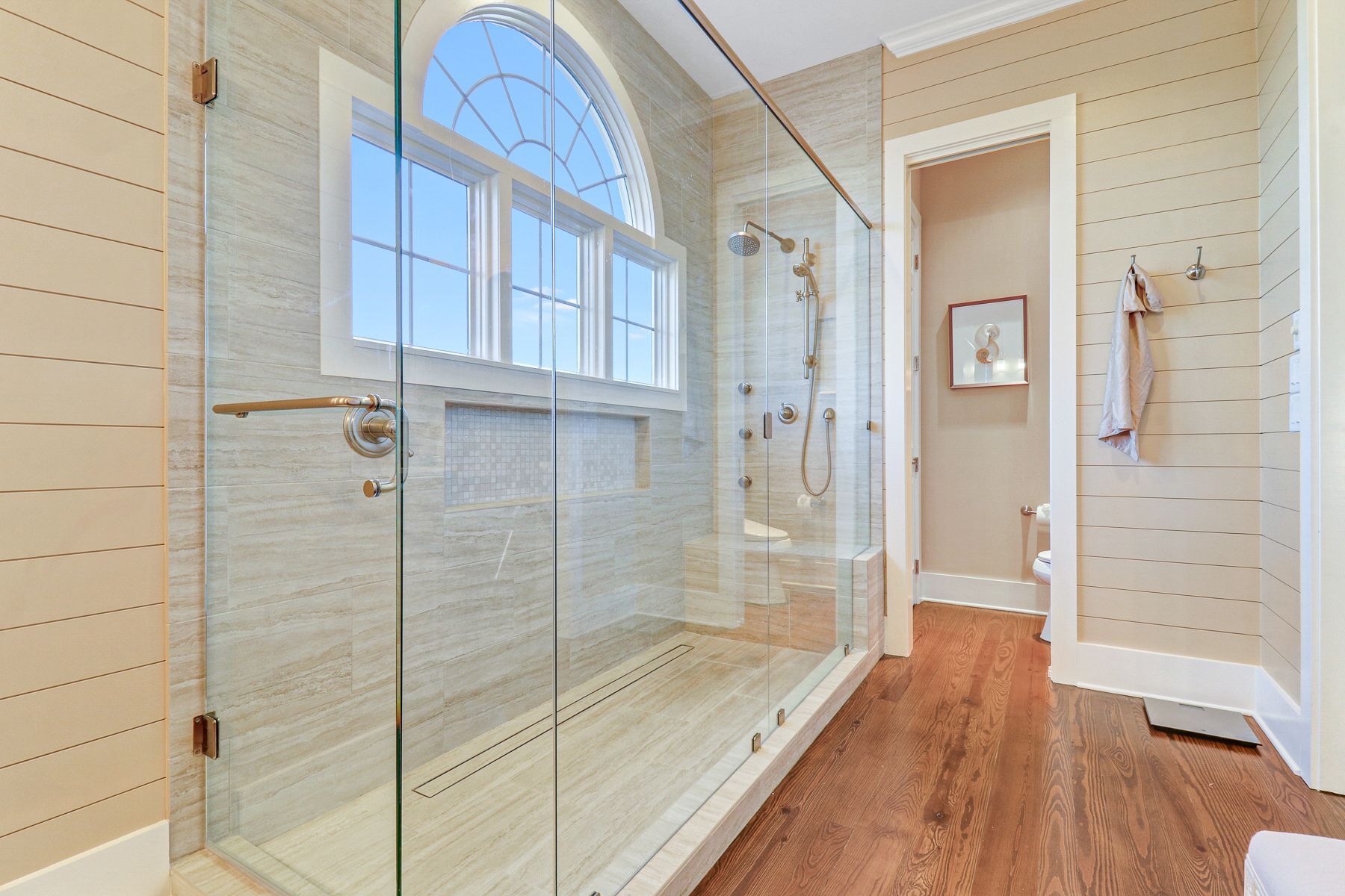 Une salle de bain moderne avec une douche à parois de verre, un plancher en bois et une grande fenêtre.