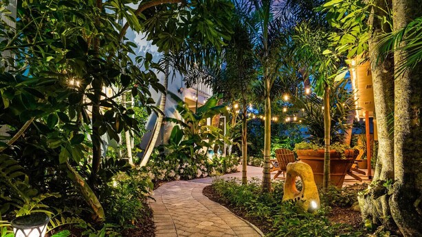 A paved garden pathway leading to a building with string lights and potted plants.