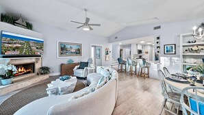 A spacious living room with a fireplace, a dining area, and a kitchen in the background.