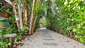 A pathway leading to a beach sign surrounded by lush greenery and tropical plants.