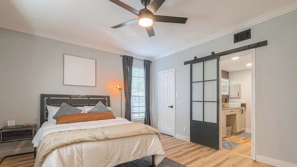 A modern bedroom with a bed, bedside tables, a ceiling fan, and a sliding door leading to a bathroom. - Cozy Oasis Apt - In Med Center & NRG (Houston)