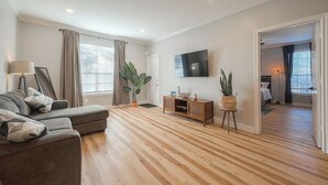 A modern living room with a sofa, TV, wooden flooring, and a plant. - Cozy Oasis Apt - In Med Center & NRG (Houston)
