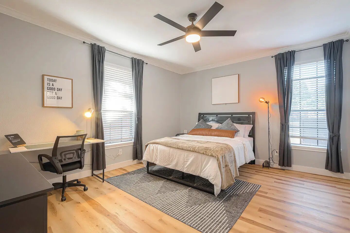 A bedroom with a bed, desk, chair, and ceiling fan.