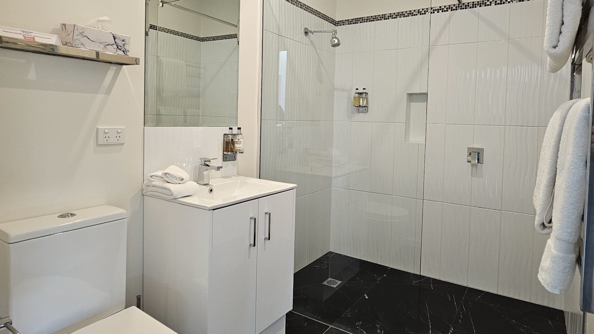 A bathroom with a white sink, mirror, and a shower area with black tiles.