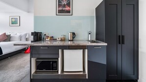 Una cocina moderna con encimera de mármol, cafetera, hervidor y microondas. Hay un armario negro con una toalla blanca colgada del tirador.