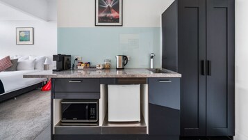 Una cocina moderna con encimera de mármol, cafetera, hervidor y microondas. Hay un armario negro con una toalla blanca colgada del tirador.
