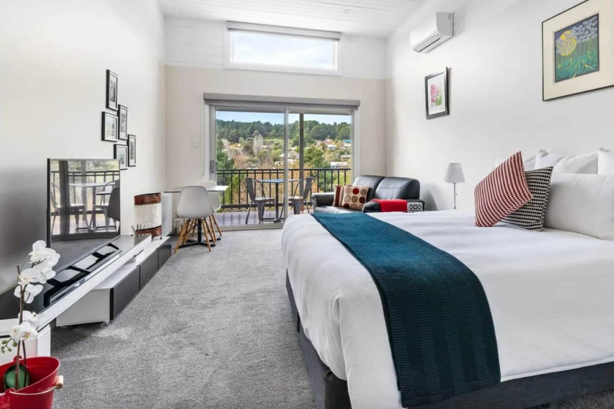 A modern hotel room with a large bed, a desk, and a balcony with a view of the city.