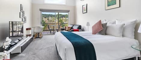 A modern hotel room with a large bed, a desk, and a balcony with a view of the city.