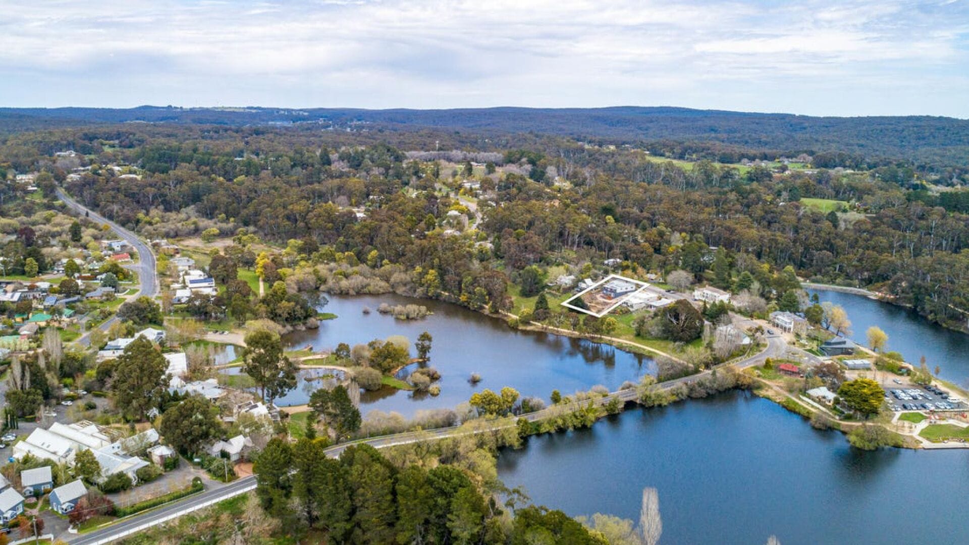 An aerial view of a lakeside community with residential areas, a bridge, and a large building complex.