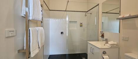 A modern bathroom with a glass shower enclosure, a white sink with a mirror, and a heated towel rail.