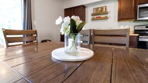 Een houten eettafel met een glazen vaas met witte bloemen op een witte onderzetter.