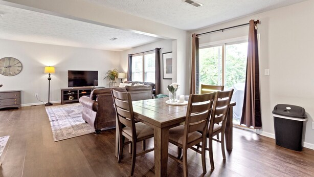 Een moderne woonkamer met een eettafel, stoelen, een bank, een televisie en een lamp.