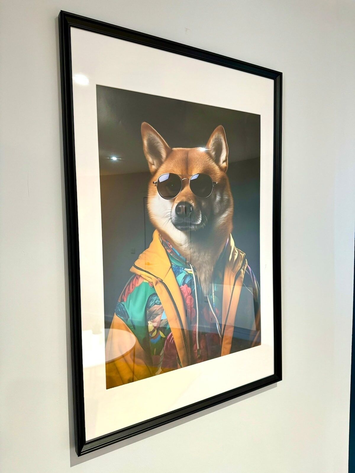 Ein gerahmtes Bild von einem Hund mit Sonnenbrille und bunter Jacke.